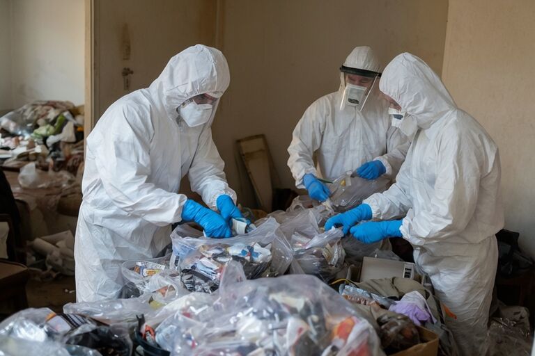 Workers in protective gear carefully sorting items during a hoarding cleanup