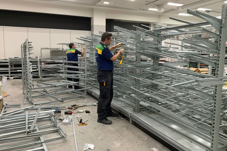 Workers dismantling and removing metal shelving racks from a retail space